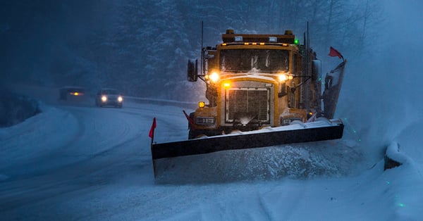 image of a semi truck with a plow, plowing a snowy road at dusk